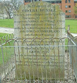 Shows a photograph of a gravestone commemorating Phoebe Hessel. A weathered stone tablet in a churchyard.