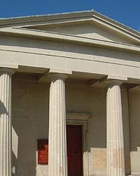 Shows a photograph of the Unitarian Church. The building resembles those of classical Greece. Three of its four pillars are shown, and it has a large red door.